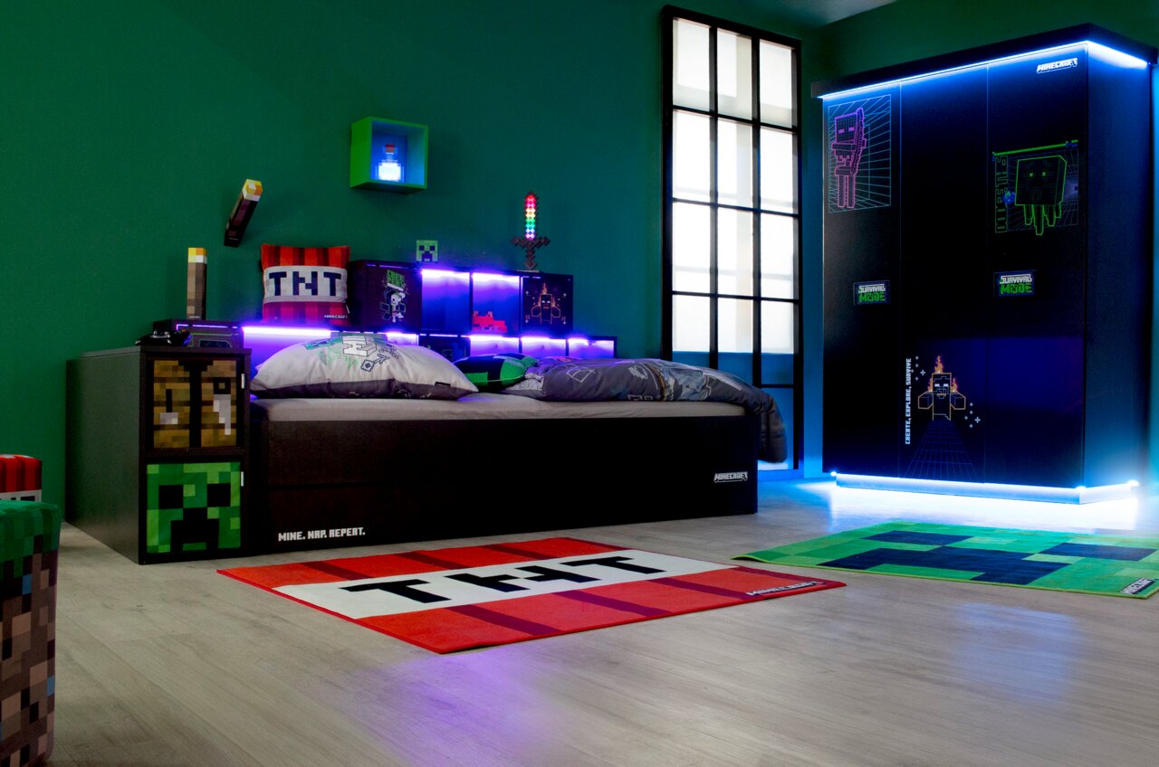 Kinderzimmer mit Gaming-Thema, zeigt einen dreitürigen Kleiderschrank mit leuchtenden Grafiken und ein Bett mit thematischer Bettwäsche, seitliche Perspektive.