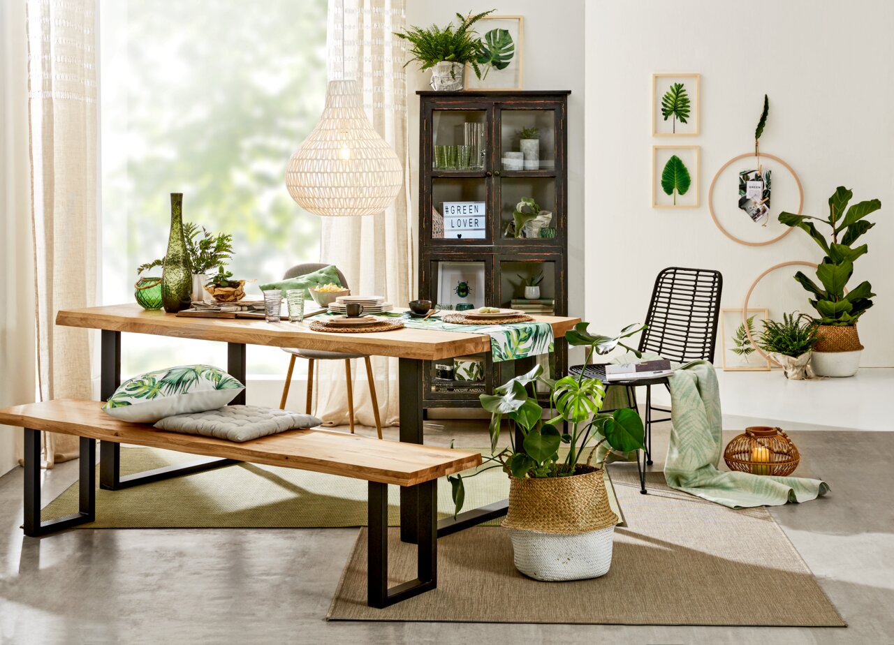 Moderner Esstisch aus Holz mit schwarzem Metallgestell, dekoriert mit grünen Pflanzen und Geschirr, seitliche Perspektive.