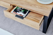 Nahaufnahme eines Couchtisches aus Holz mit schwarzem Metallgestell, einer geöffneten Schublade mit Zeitschriften und Fernbedienungen, von oben fotografiert.