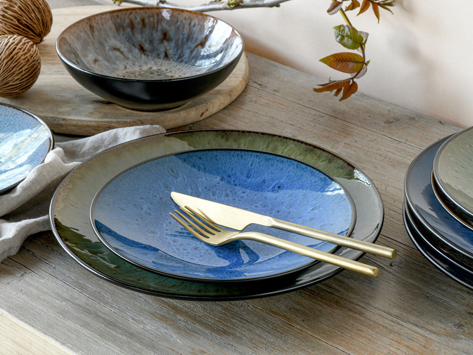 Kombiservice Bali 16-tlg. in Nahaufnahme, bestehend aus Tellern und Schalen mit blau-grüner Glasur auf einem Holztisch, goldfarbenes Besteck liegt auf einem Teller.