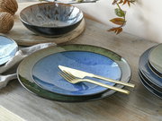 Kombiservice Bali 16-tlg. in Nahaufnahme, bestehend aus Tellern und Schalen mit blau-grüner Glasur auf einem Holztisch, goldfarbenes Besteck liegt auf einem Teller.