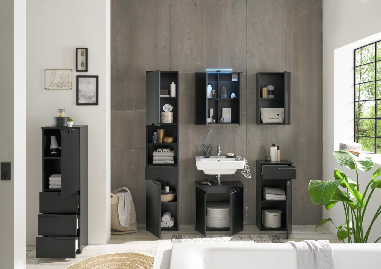 Moderner Waschbeckenunterschrank in schwarzem Design, frontal fotografiert, umgeben von weiteren Badezimmermöbeln in einem stilvollen, hellen Raum.