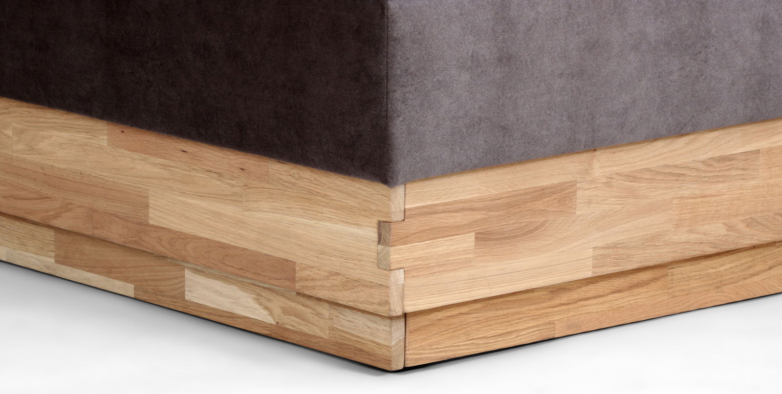 Nahaufnahme der Ecke eines Boxspringbetts mit Holzrahmen und dunklem Stoffbezug, seitliche Perspektive