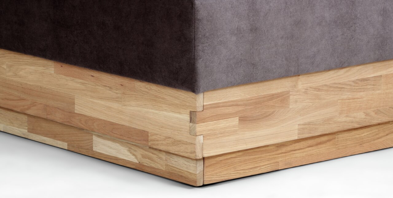 Nahaufnahme der Ecke eines Boxspringbetts mit Holzrahmen und dunklem Stoffbezug, seitliche Perspektive