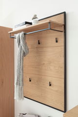 Garderobenpaneel aus Holz mit schwarzem Metallrahmen, seitliche Perspektive. Oben ein Regal mit Büchern und Flasche, darunter Haken mit Schal.