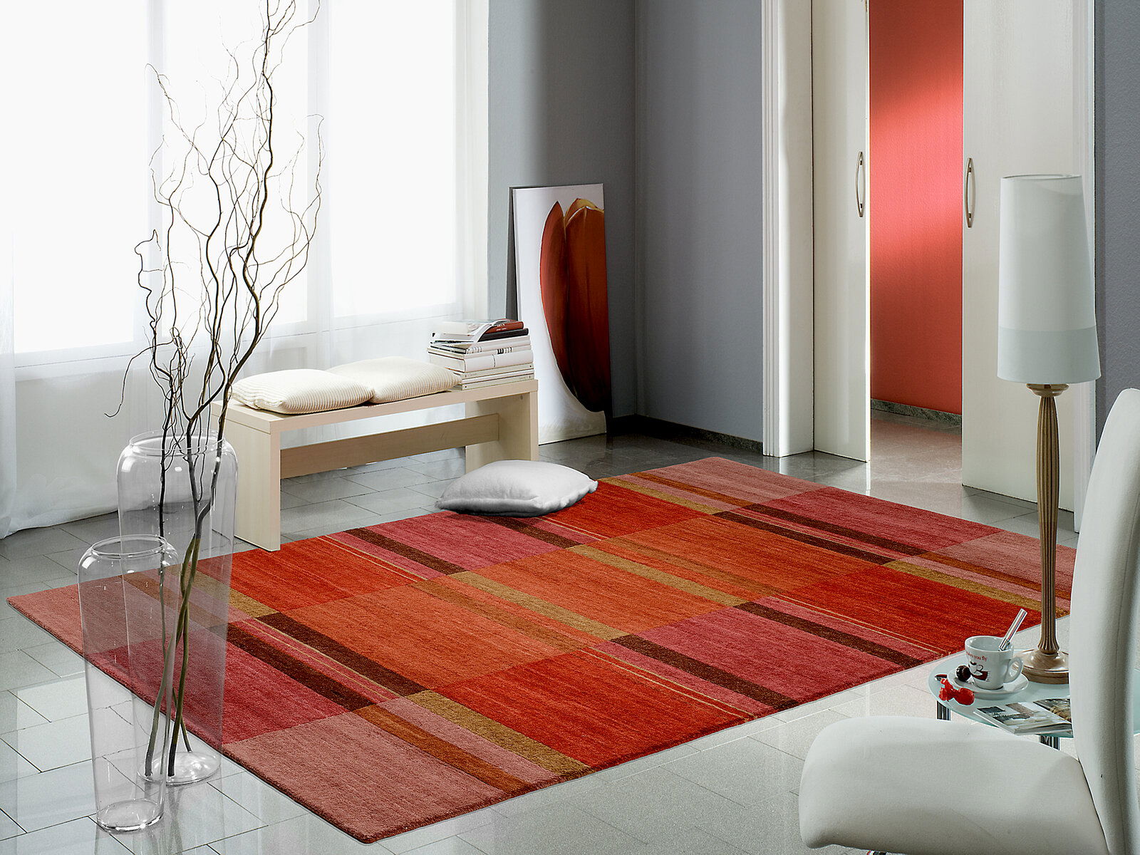 OCI Wollteppich SENSATION Moderner Wollteppich in warmen Rottönen mit Streifenmuster, auf glänzendem Fliesenboden in einem hellen Raum mit minimalistischer Einrichtung, aus der Vogelperspektive fotografiert.