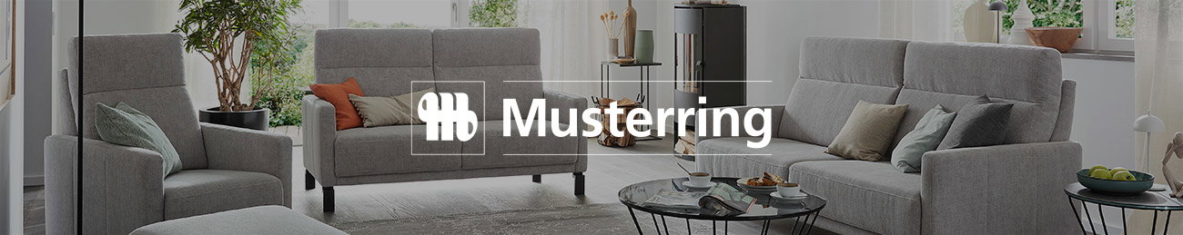 Das Bild zeigt ein Wohnzimmer mit grauen Polstermöbeln. Es gibt ein Sofa, einen Sessel und kleine Tische mit Glasplatten. Im Hintergrund stehen Pflanzen und Dekorationen. In der Mitte steht das Logo von „Musterring“.
