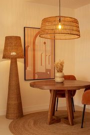 Rattan Outdoor-Stehleuchte in einem stilvoll eingerichteten Raum mit Holztisch und Kunstwerk an der Wand, seitliche Perspektive.