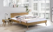 Modernes Bettgestell aus Holz in einem hellen, minimalistischen Schlafzimmer mit großen Fenstern, seitliche Perspektive.
