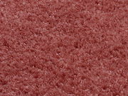 Nahaufnahme eines weichen, runden Teppichs in rötlicher Farbe, von oben betrachtet.