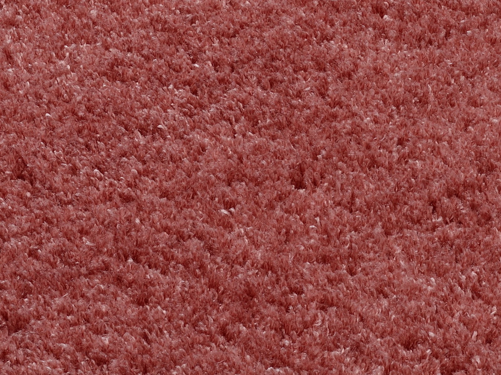 Nahaufnahme eines weichen, runden Teppichs in rötlicher Farbe, von oben betrachtet.