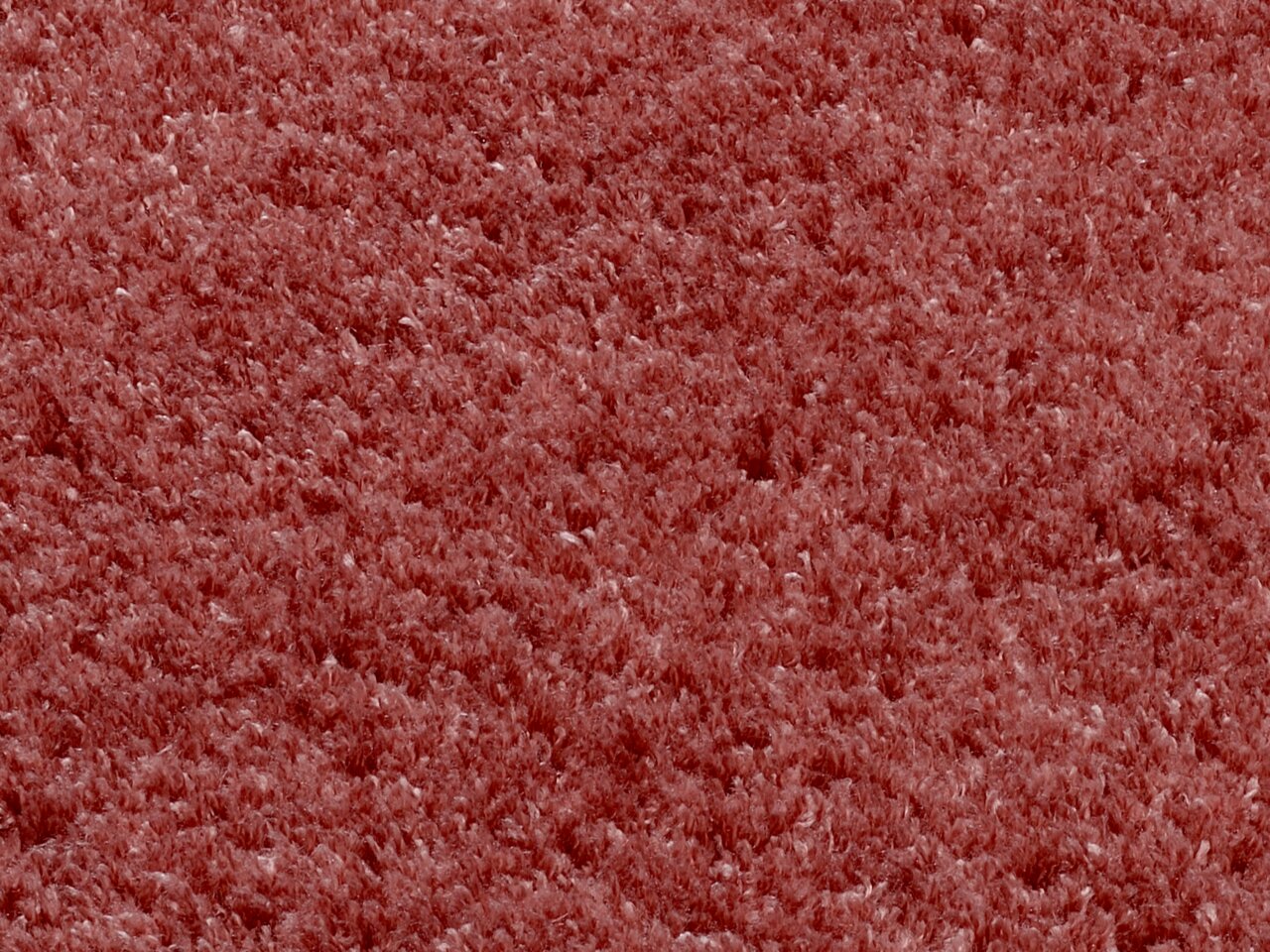 Nahaufnahme eines weichen, runden Teppichs in rötlicher Farbe, von oben betrachtet.