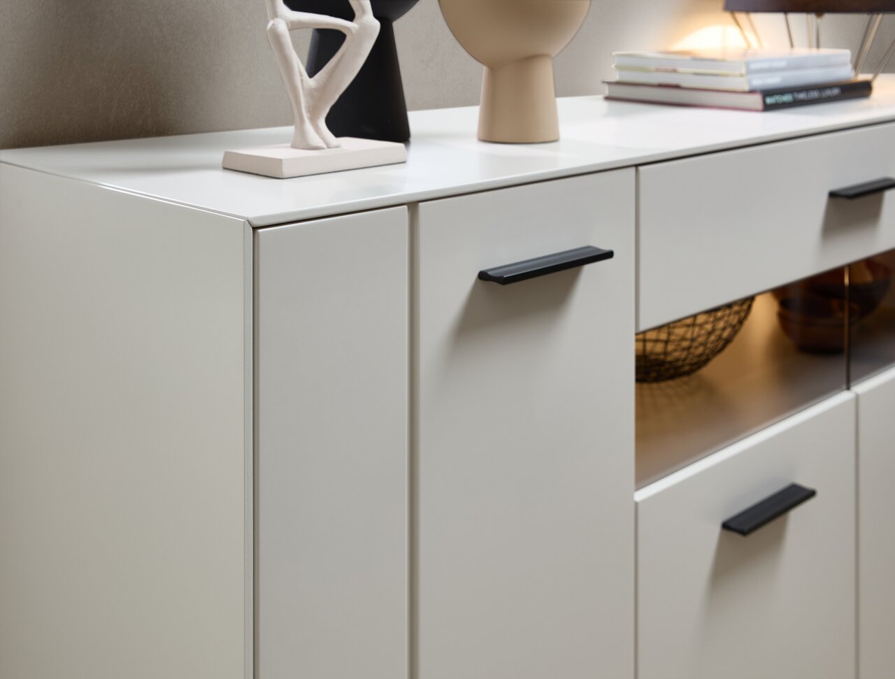 Zurbrüggen Dressoir COMO Modern dressoir in een lichte uitvoering met zwarte handgrepen, versierd met beeldjes en boeken, gezien vanaf de zijkant.