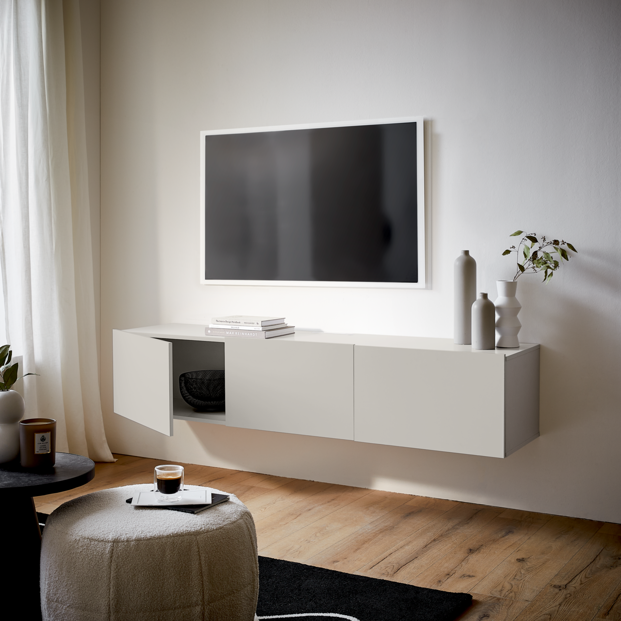 Modernes TV-Hängelowboard in Weiß, seitliche Perspektive, mit dekorativen Vasen und Pflanzen, unter einem an der Wand montierten Fernseher.