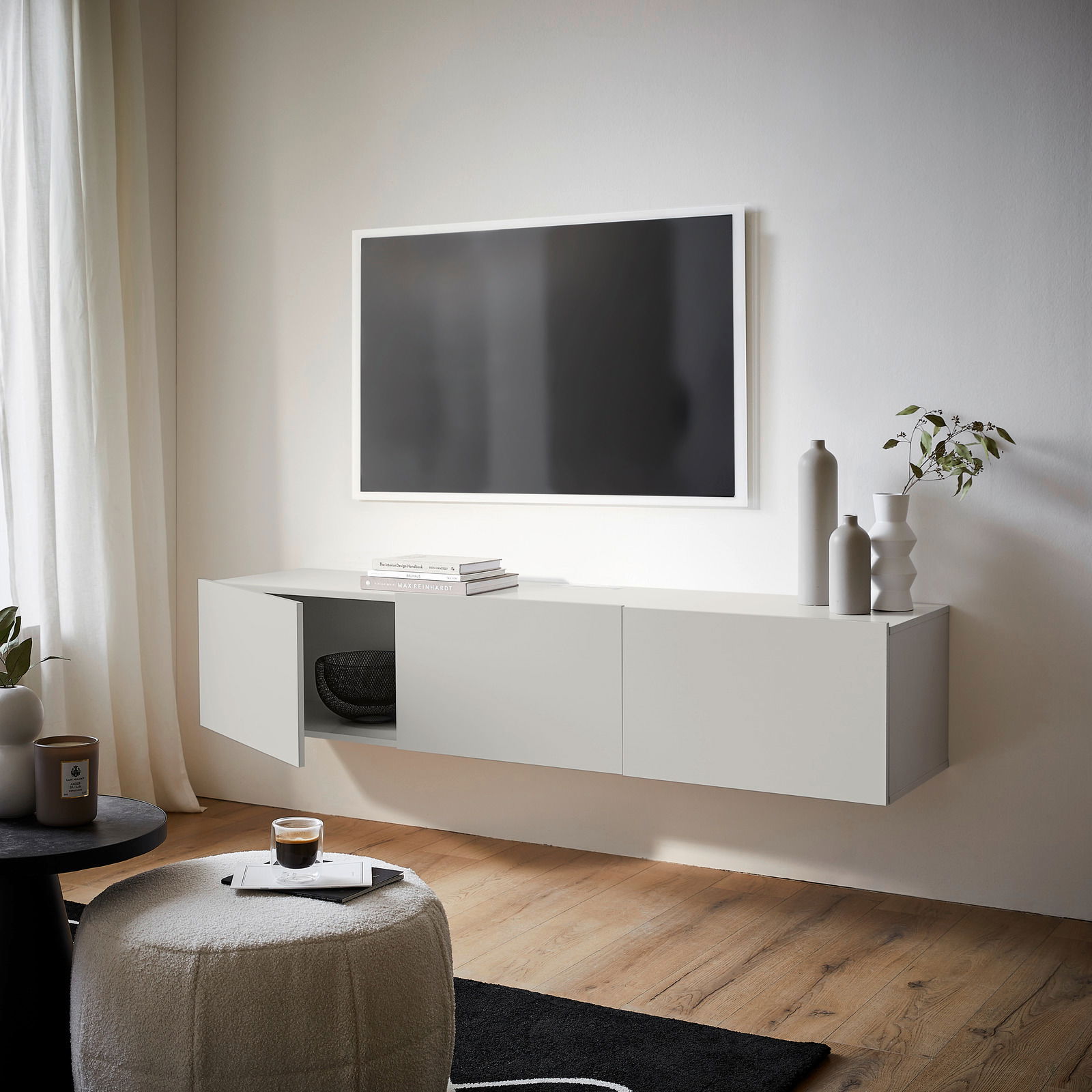 Modernes TV-Hängelowboard in Weiß, seitliche Perspektive, mit dekorativen Vasen und Pflanzen, unter einem an der Wand montierten Fernseher.