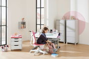 Ein moderner Jugenddrehstuhl in einem hellen, freundlichen Raum. Der Stuhl hat eine weiße Basis und eine pinke Sitzfläche. Perspektive von der Seite, mit einem Kind, das am Schreibtisch sitzt.