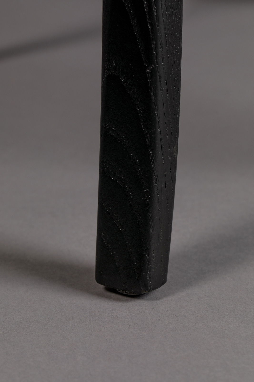 Nahaufnahme eines schwarzen Stuhlbeins auf grauem Hintergrund, von der Seite betrachtet.