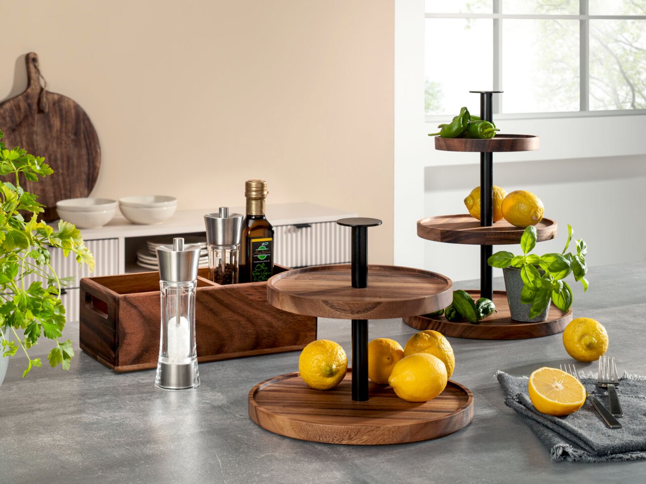 Holz-Etagere mit zwei Ebenen, dekoriert mit Zitronen und Kräutern, auf einer Küchenarbeitsplatte vor einem Fenster.