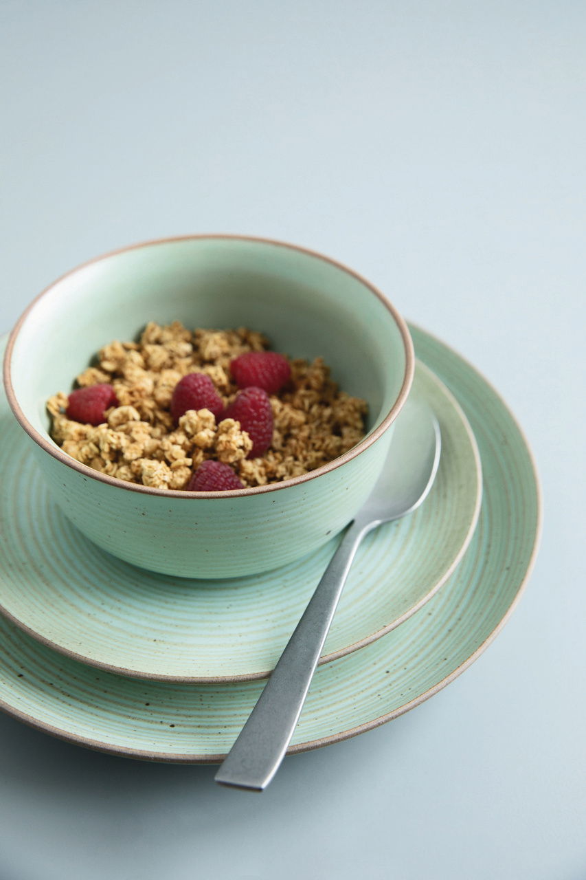 Grüner Frühstücksteller mit passender Schale, gefüllt mit Müsli und Himbeeren, von oben fotografiert.