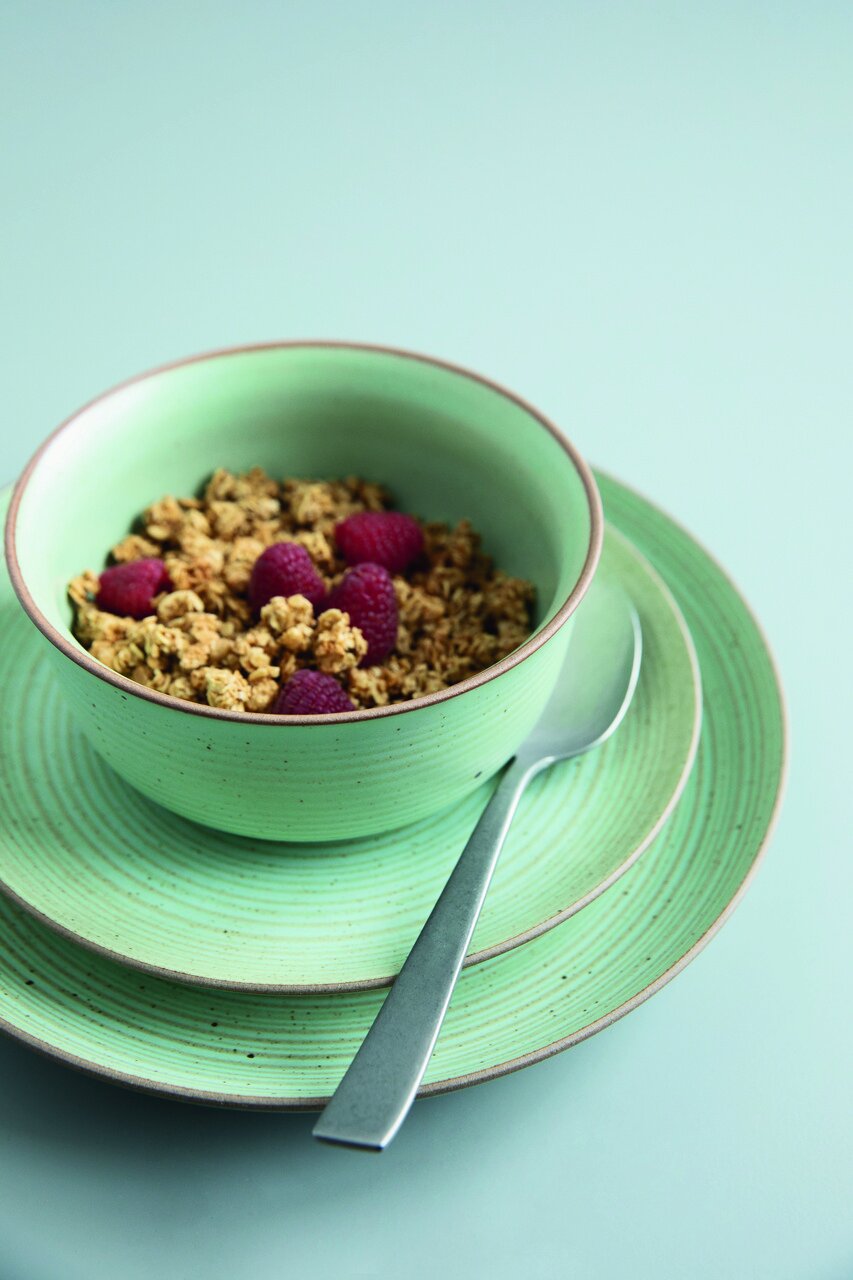 Grüner Frühstücksteller mit passender Schale, gefüllt mit Müsli und Himbeeren, von oben fotografiert.