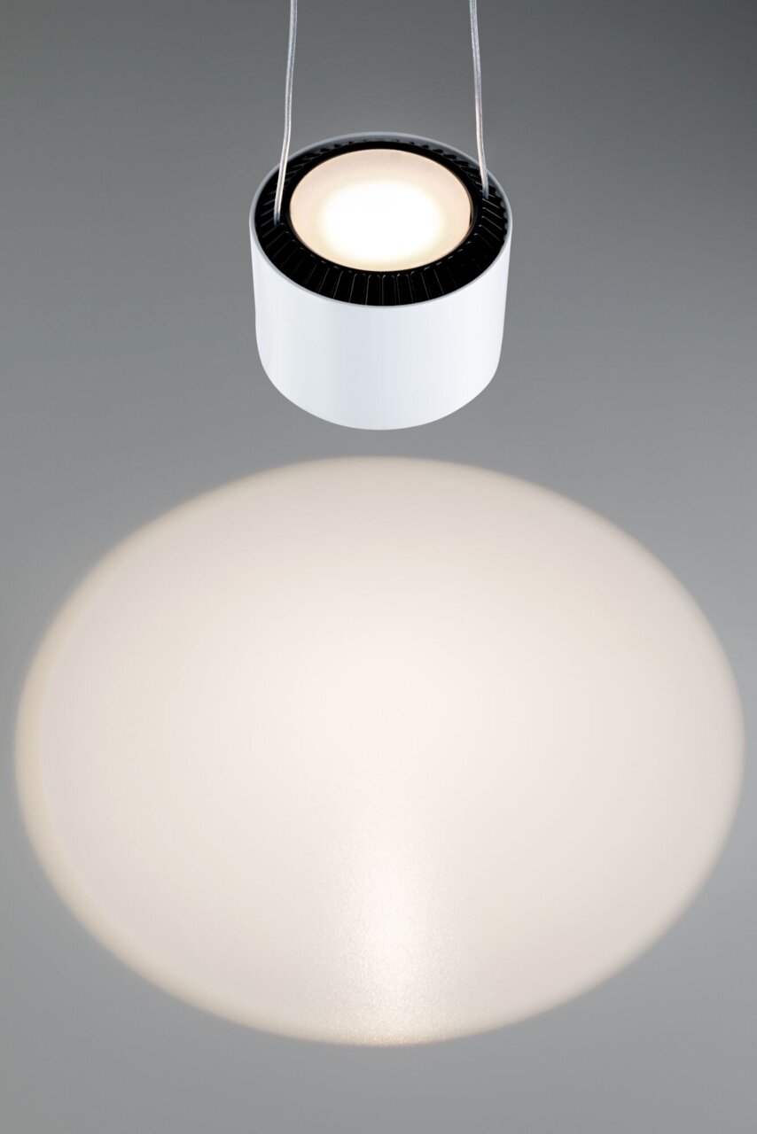 Hängende zylindrische Pendelleuchte in Weiß mit direkter Draufsicht, die einen breiten Lichtkegel auf eine graue Oberfläche wirft.