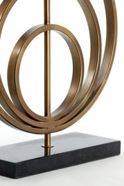 Close-up van een decoratieve metalen lampvoet met een cirkelvormig ontwerp op een rechthoekige voet, gezien vanuit de zijkant.