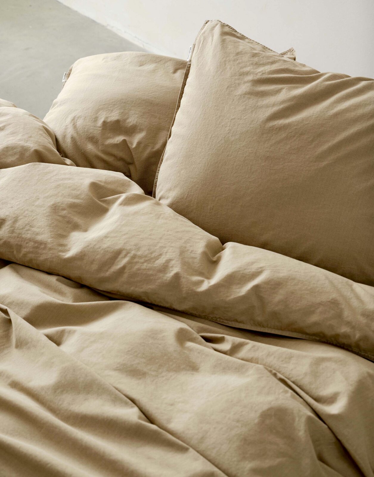 Beige Bettwäsche-Set in Nahaufnahme, bestehend aus Kissen und Decke, auf einem Bett arrangiert.