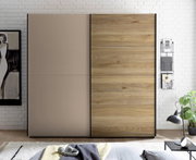 Moderner Kleiderschrank mit zwei Schiebetüren, links in Taupe und rechts in Holzoptik mit schwarzem Rahmen, frontal aus Augenhöhe im Schlafzimmer fotografiert
