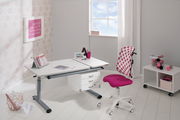 Moderner Schreibtisch in einem hellen Raum mit einem großen Fenster im Hintergrund. Der Schreibtisch hat eine weiße Oberfläche und graue Beine, ausgestattet mit Schubladen. Ein pink gepunkteter Stuhl steht davor. Perspektive: seitliche Ansicht.