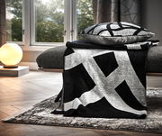 Moderne Wohndecke in Schwarz-Weiß mit geometrischem Muster, drapiert über einem Sofa in einem stilvoll eingerichteten Wohnzimmer, seitliche Perspektive.