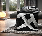 Moderne Wohndecke in Schwarz-Weiß mit geometrischem Muster, drapiert über einem Sofa in einem stilvoll eingerichteten Wohnzimmer, seitliche Perspektive.