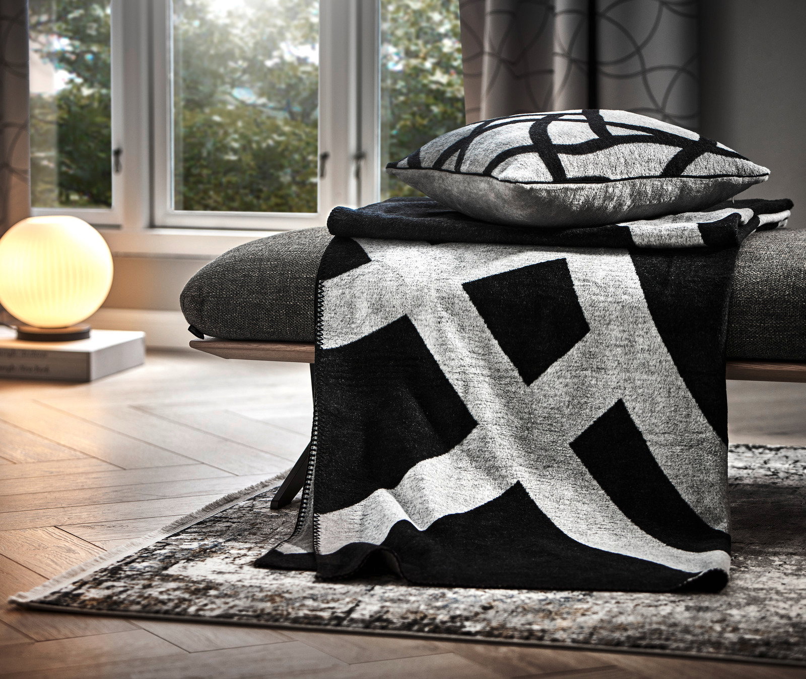Moderne Wohndecke in Schwarz-Weiß mit geometrischem Muster, drapiert über einem Sofa in einem stilvoll eingerichteten Wohnzimmer, seitliche Perspektive.