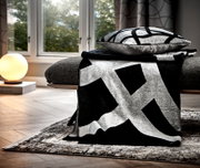 Moderne Wohndecke in Schwarz-Weiß mit geometrischem Muster, drapiert über einem Sofa in einem stilvoll eingerichteten Wohnzimmer, seitliche Perspektive.