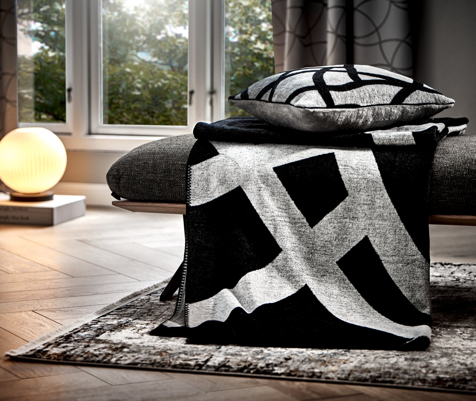 Moderne Wohndecke in Schwarz-Weiß mit geometrischem Muster, drapiert über einem Sofa in einem stilvoll eingerichteten Wohnzimmer, seitliche Perspektive.