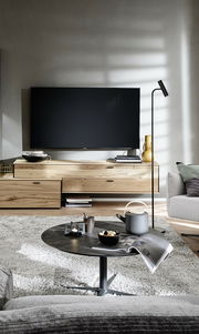 Moderne Wandkombination ANDRA in hellem Holz mit integriertem Fernseher, von vorne betrachtet. Stilvolle Dekorationen und ein gemütlicher Wohnbereich im Vordergrund.