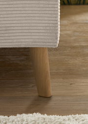 Nahaufnahme eines Polsterbettes mit Holzbein auf Holzboden, seitliche Perspektive