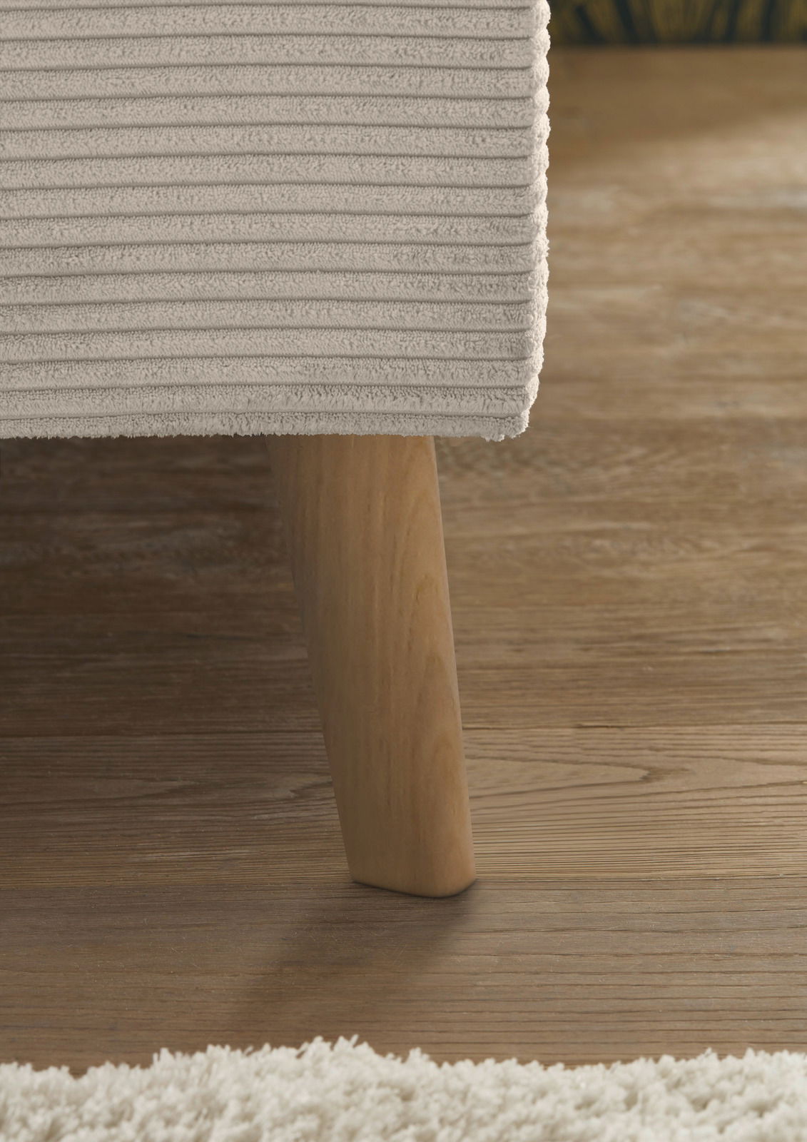 Nahaufnahme eines Polsterbettes mit Holzbein auf Holzboden, seitliche Perspektive