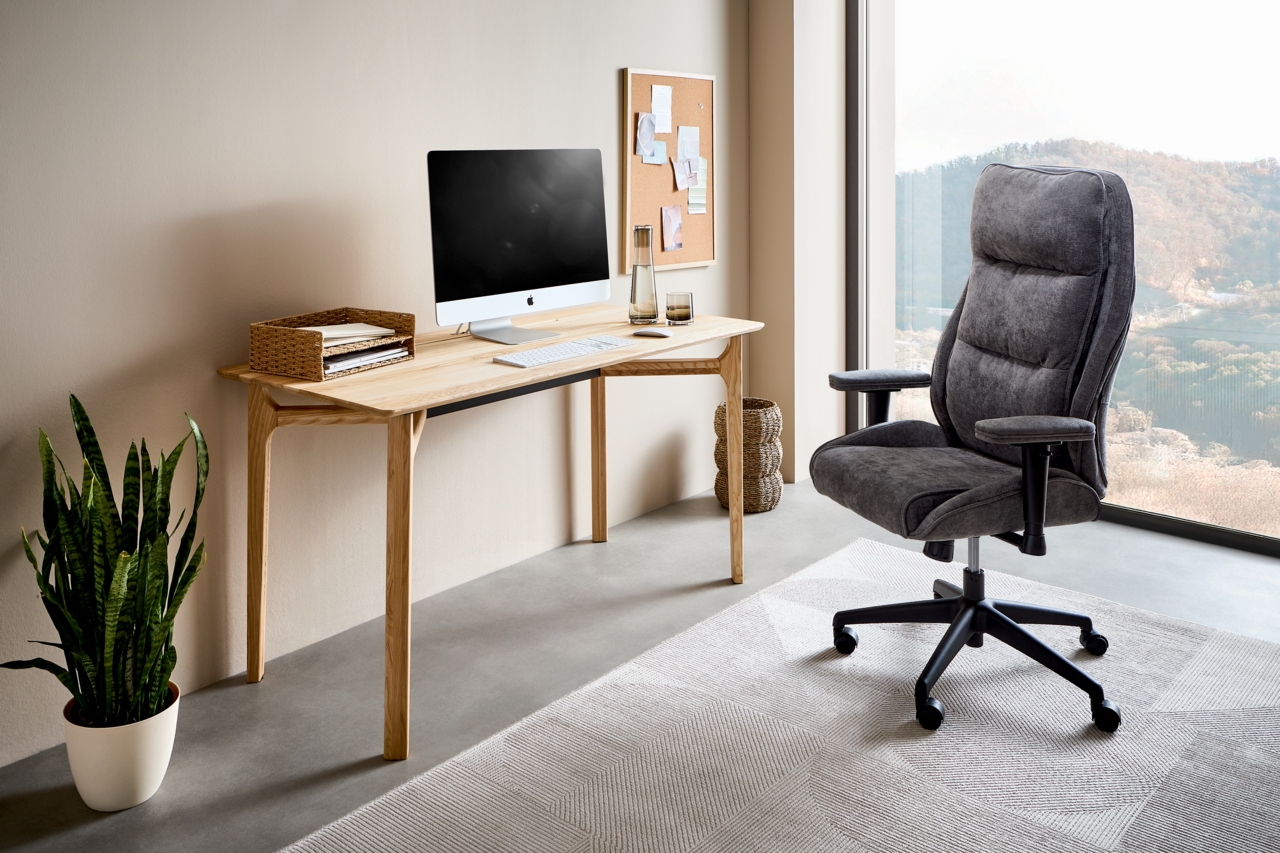 Moderner Schreibtisch aus Holz mit Computer, Pflanzen und ergonomischem Bürostuhl in einem hellen Raum mit großem Fenster, seitliche Perspektive.