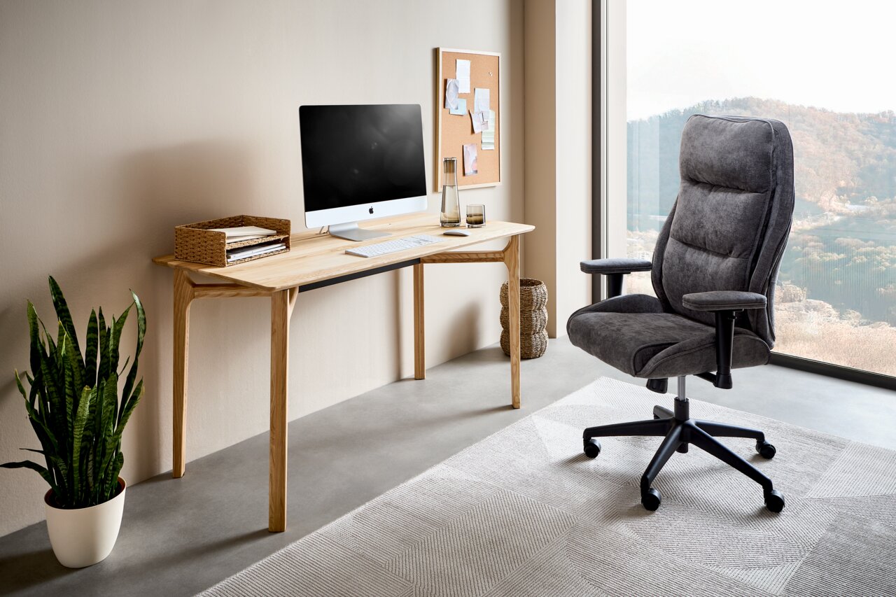 Moderner Schreibtisch aus Holz mit Computer, Pflanzen und ergonomischem Bürostuhl in einem hellen Raum mit großem Fenster, seitliche Perspektive.