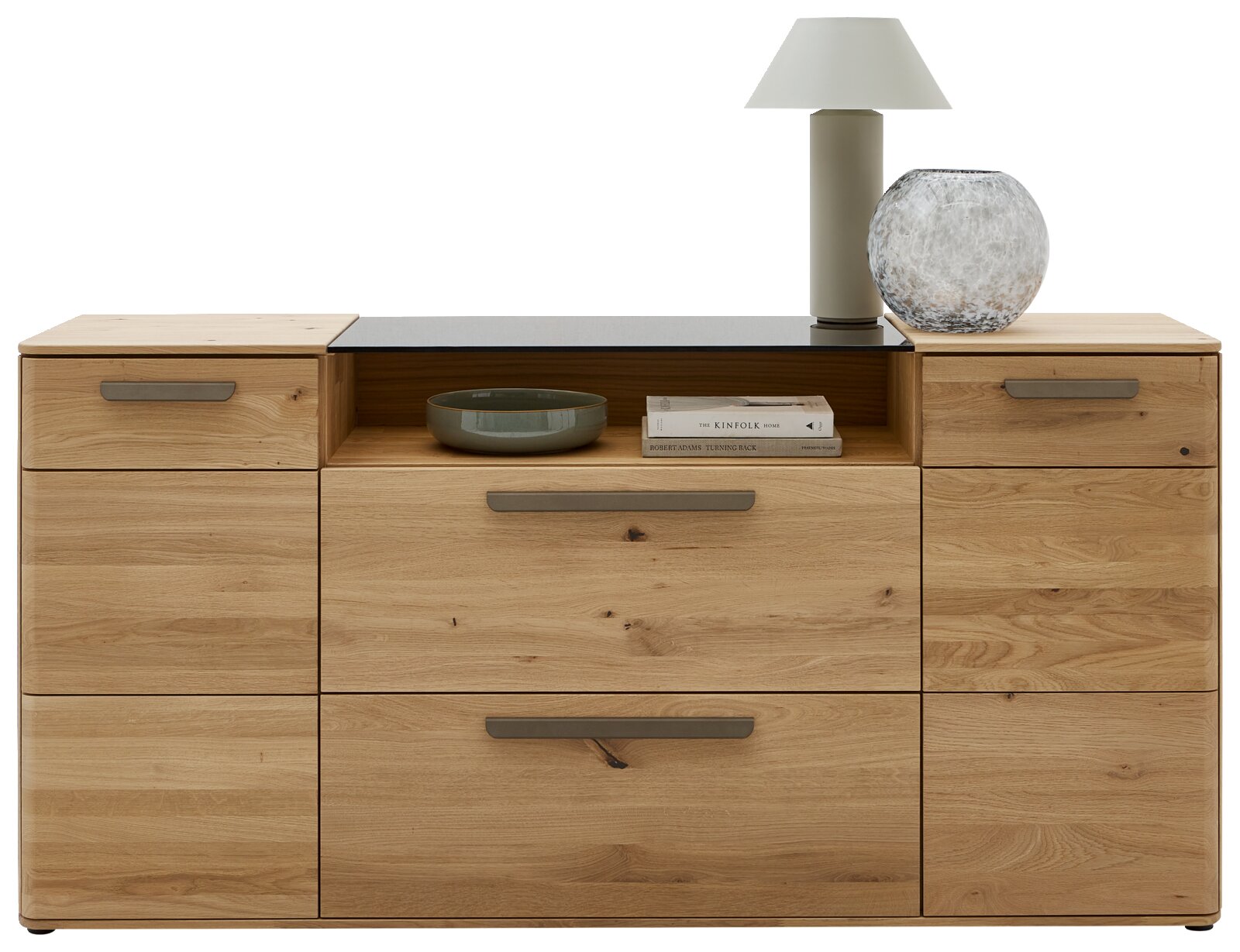 Frontansicht einer modernen Kommode aus hellem Massivholz mit mehreren Schubladen, mittigem offenen Fach und grauen Griffleisten, dekoriert mit Lampe, Glasvase, Schale und Büchern auf weißem Hintergrund