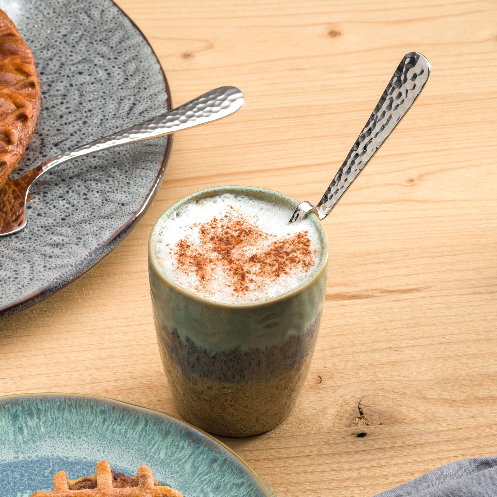 Leonardo Latte Macchiato Löffel Gebogener Latte Macchiato Löffel aus Edelstahl in einer Tasse mit Milchschaum, von oben fotografiert.