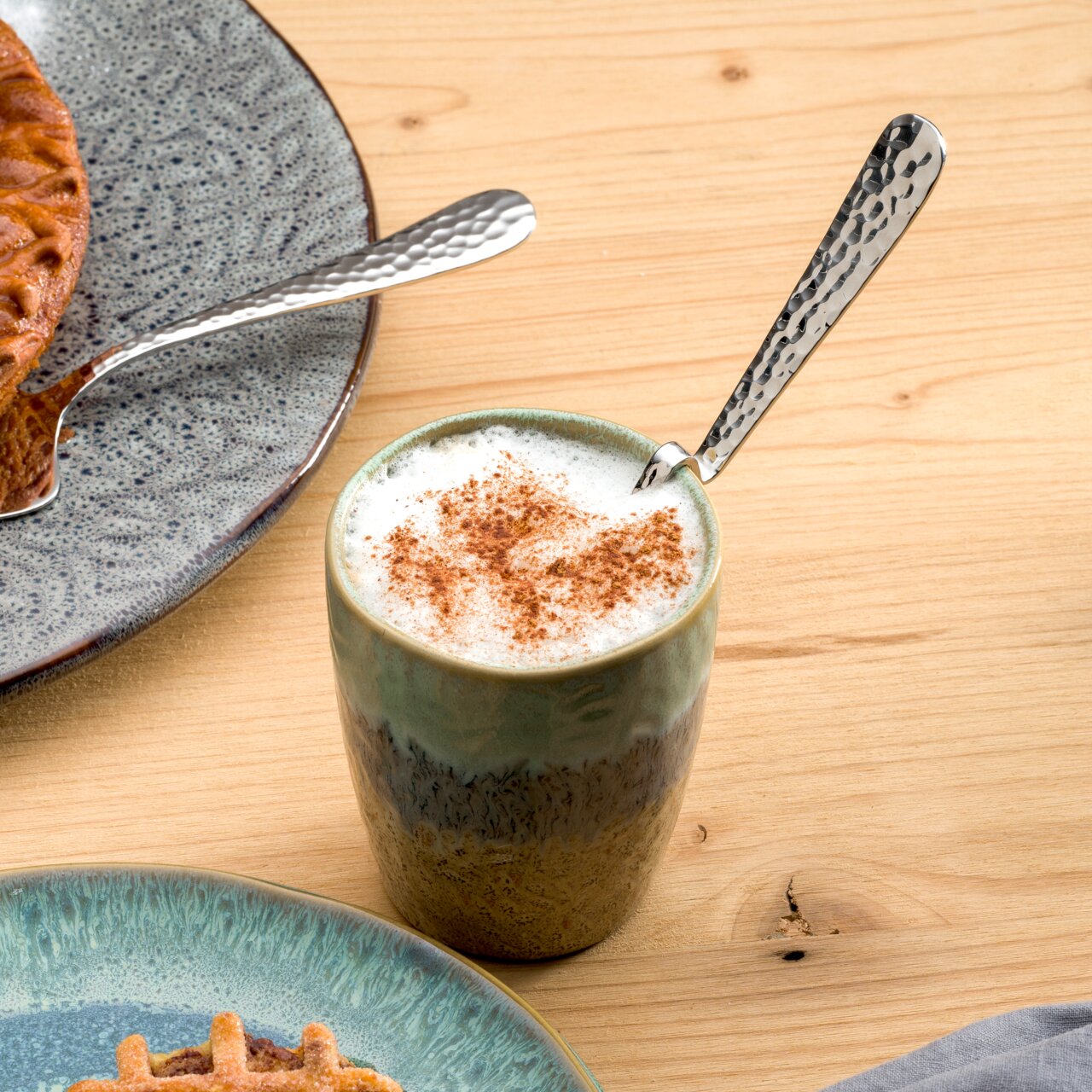 Een gebogen latte macchiato-lepel van roestvrij staal in een kopje met melkschuim, gefotografeerd van bovenaf.