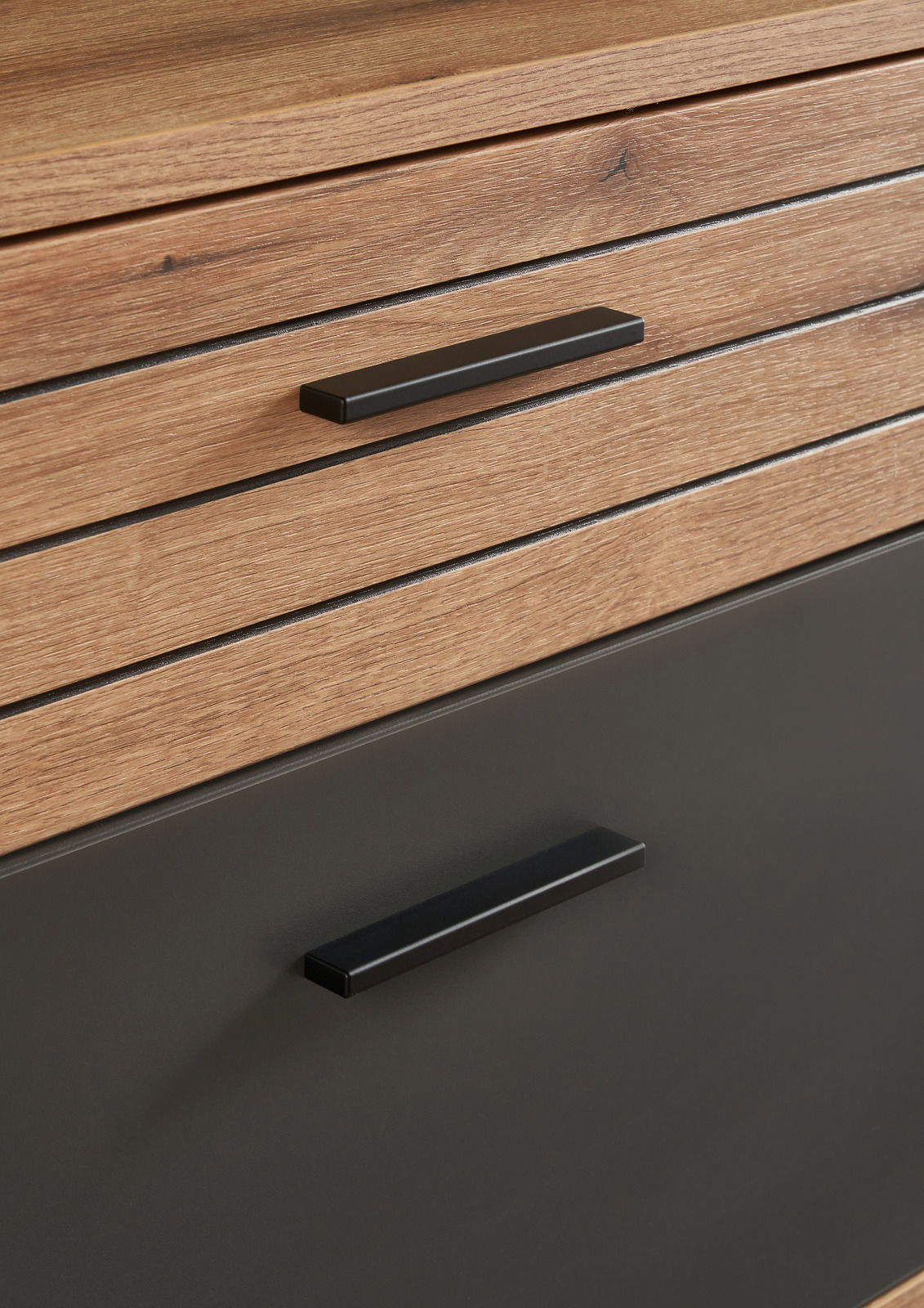 Nahaufnahme eines Möbelstücks mit Holzoptik und schwarzen Griffen, perspektivisch von vorne aufgenommen.