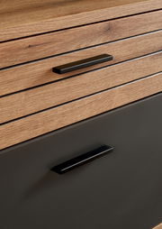 Nahaufnahme eines Möbelstücks mit Holzoptik und schwarzen Griffen, perspektivisch von vorne aufgenommen.