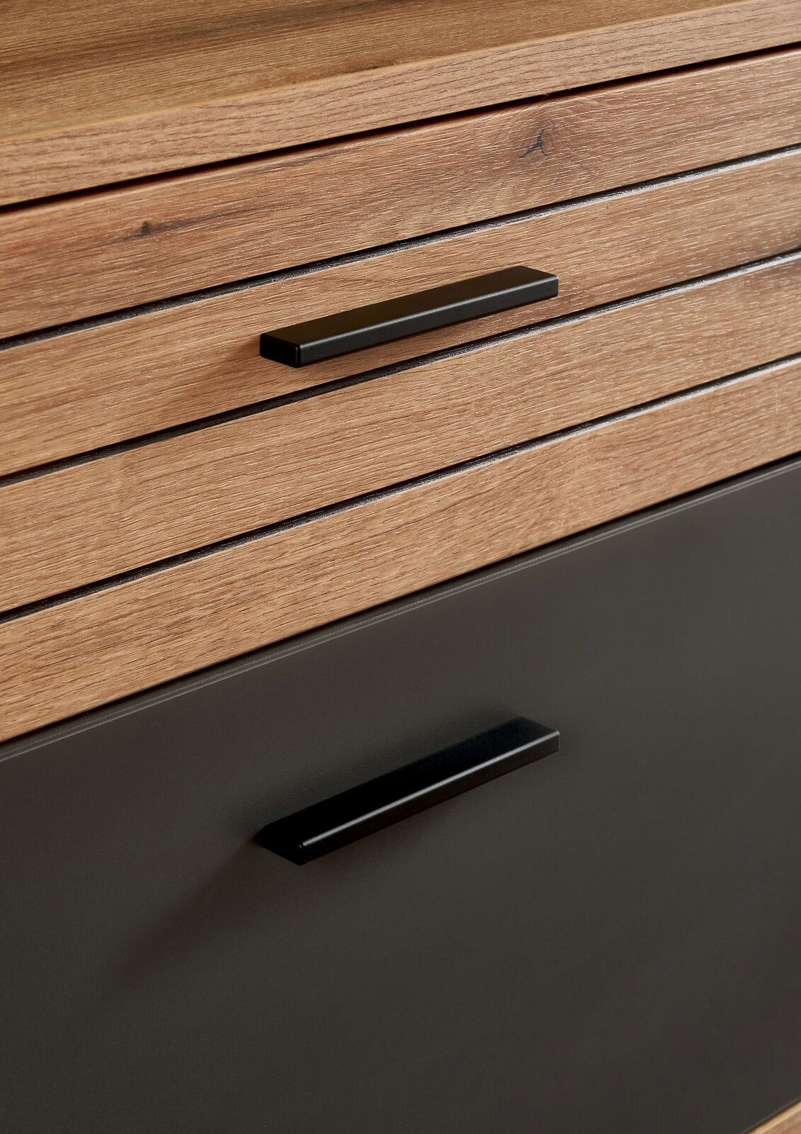 Nahaufnahme eines Möbelstücks mit Holzoptik und schwarzen Griffen, perspektivisch von vorne aufgenommen.
