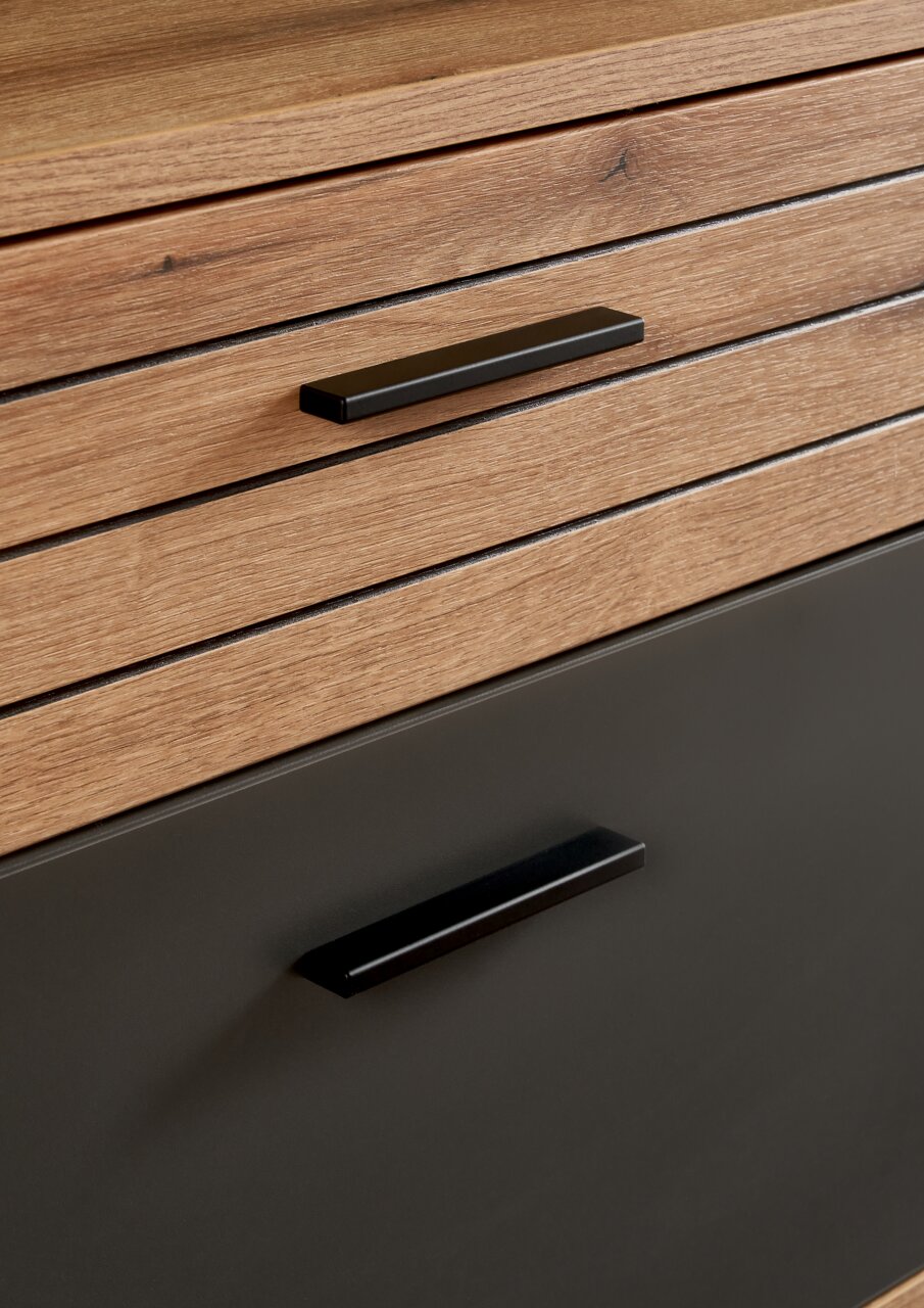 Nahaufnahme eines Möbelstücks mit Holzoptik und schwarzen Griffen, perspektivisch von vorne aufgenommen.