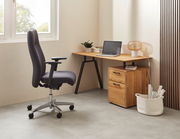 Bürostuhl in Seitenansicht neben einem Schreibtisch mit Laptop und Lampe, in einem modernen Büro.