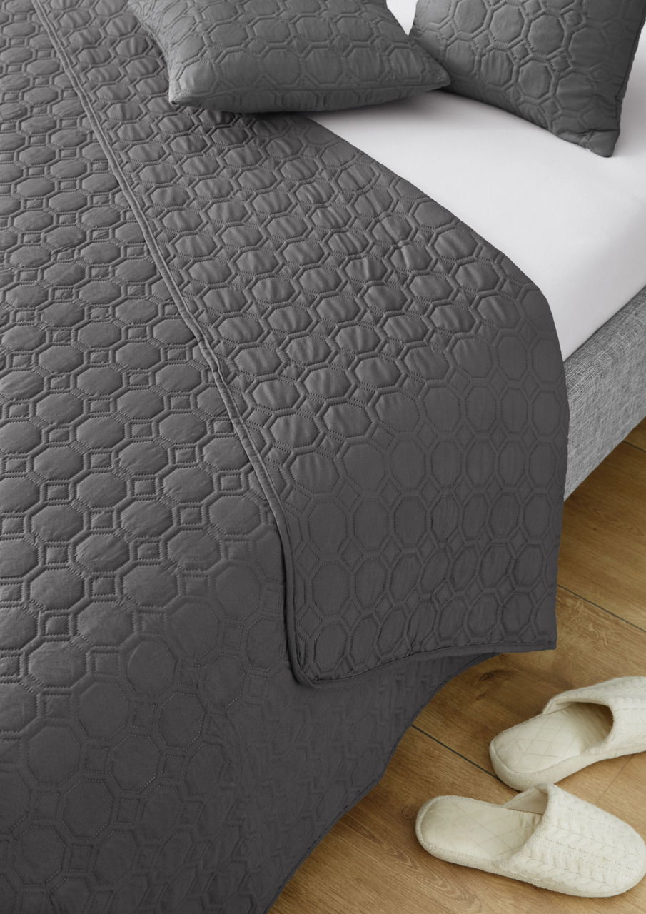 Graue Tagesdecke Nancy 220x250cm mit geometrischem Muster, auf einem Bett drapiert, aus der Vogelperspektive fotografiert.