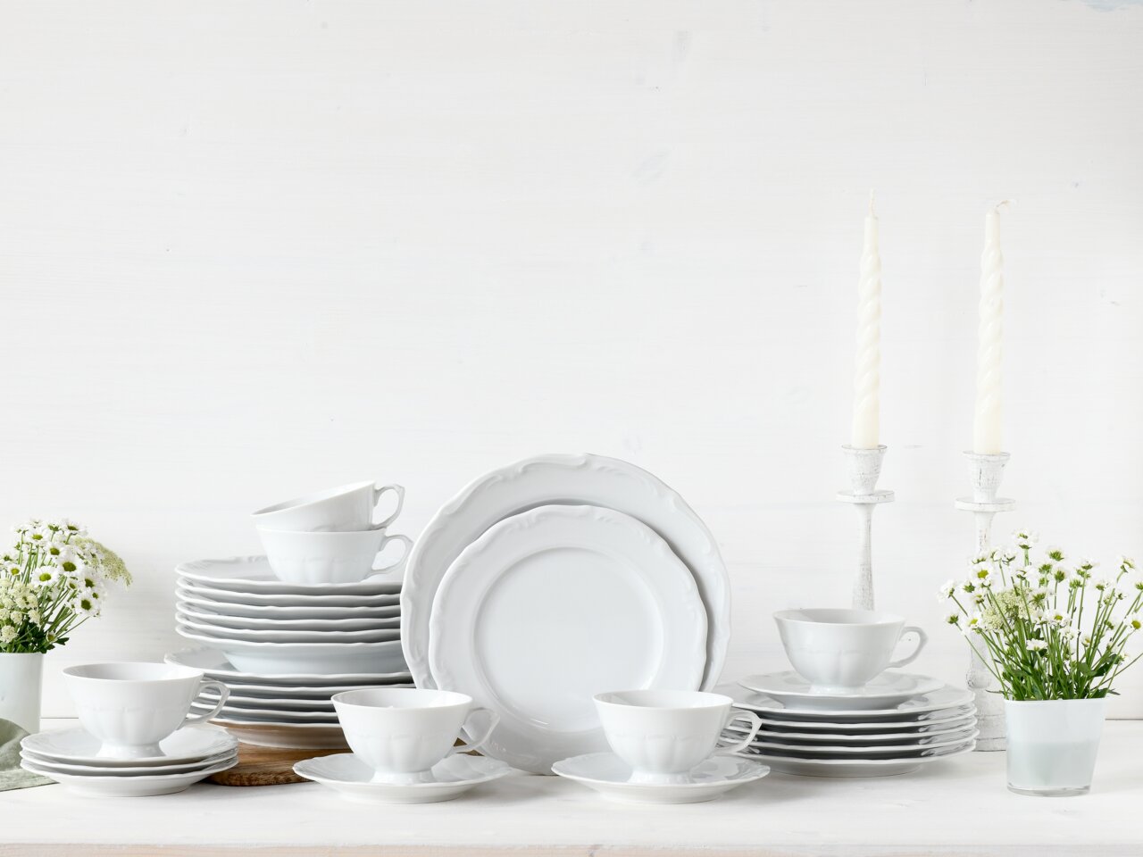 Het elegante witte servies Maria Theresia 30 met kopjes, borden en schoteltjes, stijlvol gerangschikt in een vooraanzicht, omringd door witte kaarsen en bloemen.