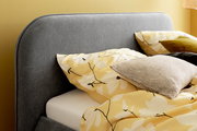 Graues Polsterbett mit gelber Blumenbettwäsche und Kissen, seitliche Perspektive